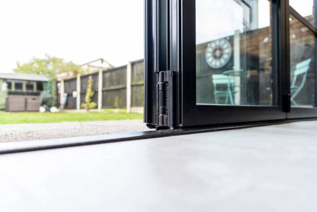 Close-up of an open glass patio door with a view of a backyard garden, including a fence, grass, and outdoor furniture.