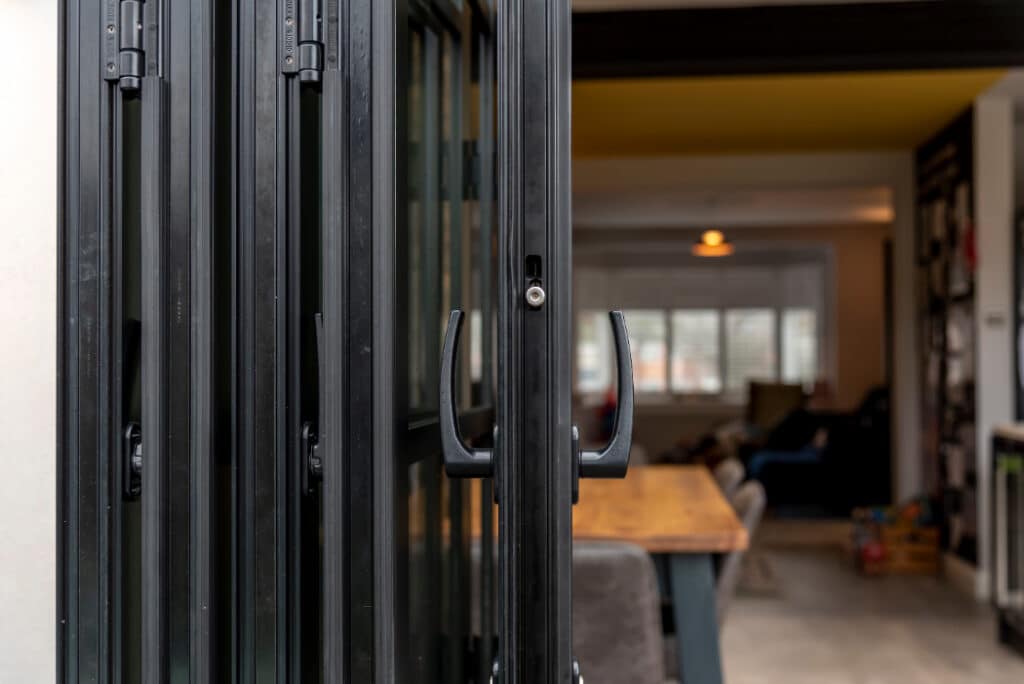 Close-up of black folding doors leading to a modern, cozy room with a dining table and chairs.
