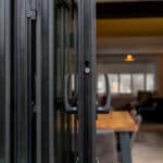 Thumbnail of http://Close-up%20of%20black%20folding%20doors%20leading%20to%20a%20modern,%20cozy%20room%20with%20a%20dining%20table%20and%20chairs.