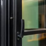 Thumbnail of http://Close-up%20of%20a%20partially%20open%20glass%20door%20with%20a%20black%20metal%20frame%20and%20handle,%20showing%20a%20blurred%20interior%20background.