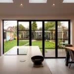 Thumbnail of http://Modern%20kitchen%20with%20a%20white%20island%20and%20black%20induction%20cooktop.%20Brick%20wall%20with%20a%20wooden%20table%20and%20chairs.%20Glass%20doors%20open%20to%20a%20backyard%20with%20a%20path,%20shed,%20and%20colorful%20mural.