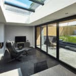 Thumbnail of http://Modern%20living%20room%20with%20large%20glass%20doors%20leading%20to%20a%20patio.%20It%20features%20a%20black%20leather%20chair,%20a%20small%20TV,%20and%20a%20visible%20fireplace.%20Sunlight%20enters%20through%20skylights.