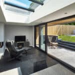 Thumbnail of http://Modern%20room%20with%20a%20sleek%20black%20chair,%20flat-screen%20TV,%20and%20fireplace.%20Glass%20sliding%20doors%20open%20to%20a%20patio%20with%20a%20chair%20and%20grass%20area%20outside.%20Ceiling%20windows%20bring%20in%20natural%20light.