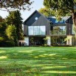 Thumbnail of http://Modern%20two-story%20house%20with%20large%20glass%20windows,%20surrounded%20by%20trees%20and%20a%20well-kept%20lawn.