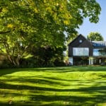 Thumbnail of http://Modern%20two-story%20house%20with%20large%20glass%20windows,%20surrounded%20by%20lush%20green%20trees%20and%20a%20well-maintained%20lawn%20on%20a%20sunny%20day.