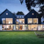 Thumbnail of http://Modern%20two-story%20house%20with%20large%20glass%20windows%20and%20navy%20siding,%20featuring%20a%20spacious%20lawn%20and%20a%20hanging%20swing%20in%20the%20foreground.