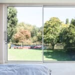 Thumbnail of http://View%20from%20a%20bedroom%20with%20a%20bed%20and%20nightstand,%20looking%20through%20large%20glass%20doors%20toward%20a%20lush%20green%20lawn,%20trees,%20and%20a%20canal%20boat%20in%20the%20background.