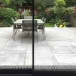 Thumbnail of http://A%20glass%20door%20opens%20to%20a%20patio%20with%20a%20table%20and%20six%20chairs.%20The%20area%20is%20surrounded%20by%20greenery%20and%20wooden%20fencing,%20with%20garden%20tools%20visible%20in%20the%20background.