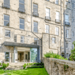 Thumbnail of http://Historic%20stone%20building%20with%20a%20modern%20glass%20extension,%20overlooking%20a%20neatly%20manicured%20garden%20and%20stone%20pathway.