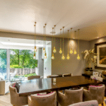 Thumbnail of http://Modern%20dining%20area%20with%20a%20large%20table,%20hanging%20pendant%20lights,%20upholstered%20chairs,%20and%20a%20landscape%20painting.%20Glass%20doors%20reveal%20a%20green%20outdoor%20view.