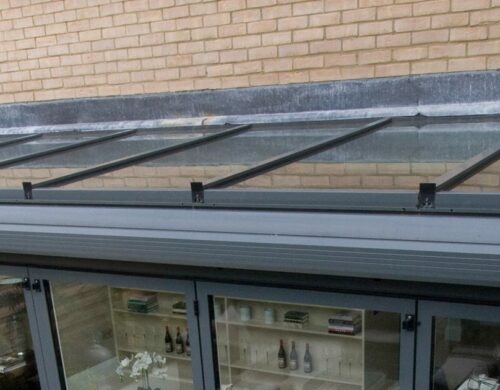 Modern lean-to glass roof with dark aluminium frame and multiple glazed panels mounted above brick building extension.