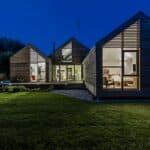 Thumbnail of http://This%20modern,%20flood-resilient%20house%20boasts%20three%20sections%20with%20expansive%20glass%20windows%20and%20wooden%20paneling,%20beautifully%20illuminated%20at%20night.%20It%20stands%20gracefully%20amidst%20a%20dark%20lawn%20and%20trees,%20harmoniously%20blending%20form%20and%20function%20for%20sustainable%20living.