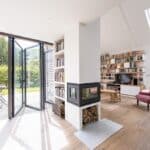 Thumbnail of http://Bright%20modern%20living%20room%20with%20flood-resilient%20wooden%20flooring,%20a%20two-sided%20fireplace,%20bookshelves,%20a%20red%20armchair,%20and%20open%20glass%20doors%20leading%20to%20a%20patio%20with%20outdoor%20seating%20and%20a%20view%20of%20the%20garden.