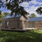 Thumbnail of http://A%20modern,%20flood-resilient%20single-story%20wooden%20house%20with%20a%20blue%20metal%20roof%20stands%20proudly%20amid%20a%20grassy%20lawn%20and%20trees%20under%20a%20partly%20cloudy%20sky.