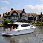Thumbnail of http://A%20white%20motorboat%20gracefully%20glides%20along%20the%20river,%20passing%20a%20charming,%20traditional-style%20house%20with%20a%20steep%20roof%20and%20black-and-white%20facade,%20under%20a%20partly%20cloudy%20sky.