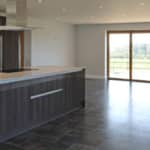 Thumbnail of http://Modern%20kitchen%20with%20a%20large%20island%20and%20dark%20cabinetry,%20featuring%20tile%20flooring%20and%20a%20glass%20door%20leading%20to%20an%20outdoor%20view.
