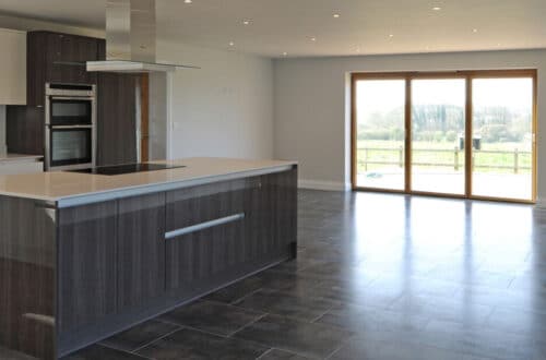 Modern kitchen with a large island and dark cabinetry, featuring tile flooring and a glass door leading to an outdoor view.
