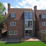 Thumbnail of http://A%20modern%20red-brick%20house%20with%20large%20front%20windows,%20a%20small%20wooden%20deck,%20and%20fenced%20backyard%20with%20grass.