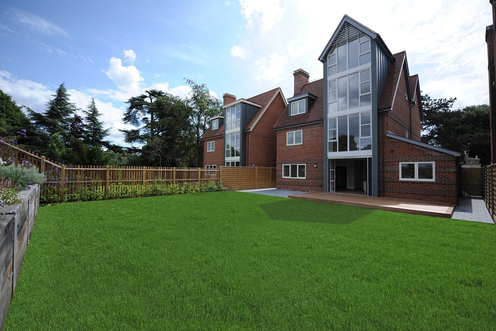 Spacious backyard with lush grass in front of a modern, multi-story brick house featuring large windows and a wooden deck.