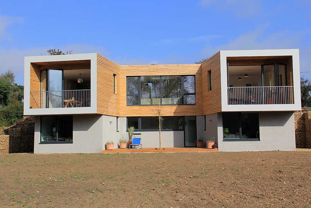 This modern two-story house features sf75 bifold doors, large windows, and wooden exterior sections with balconies. The front yard is bare soil, while potted plants adorn the entrance, adding a touch of greenery.