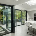Thumbnail of http://Modern%20kitchen%20with%20white%20cabinets%20and%20island,%20glass%20doors%20opening%20to%20a%20garden%20view.%20Skylight%20above,%20tiled%20floor,%20and%20barstool%20seating.
