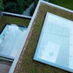 Thumbnail of http://Two%20rooftop%20windows%20on%20a%20green%20roof%20with%20grass%20and%20plants,%20overlooking%20a%20room%20below.