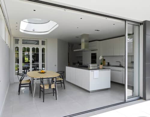 Modern kitchen with white cabinets, an island with a gray countertop, and a dining area. Skylight above and sliding glass doors open to the outside. Black chairs surround a wooden table.
