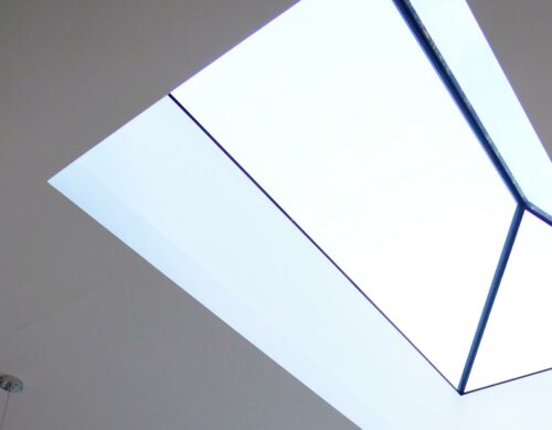 Interior view of a frameless glass roof lantern with blue structural framing, allowing natural light through the glazed panels against a neutral ceiling.