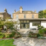 Thumbnail of http://A%20two-story%20house%20with%20a%20mix%20of%20stone%20and%20modern%20white%20exteriors,%20surrounded%20by%20a%20garden%20with%20trees%20and%20shrubs,%20under%20a%20clear%20blue%20sky.