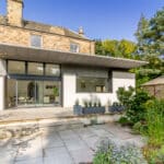 Thumbnail of http://Modern%20extension%20on%20a%20stone%20house%20with%20large%20windows,%20a%20patio,%20and%20a%20landscaped%20garden%20featuring%20various%20plants%20and%20trees%20under%20a%20clear%20blue%20sky.