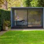 Thumbnail of http://A%20small%20modern%20garden%20office%20with%20glass%20walls,%20featuring%20a%20desk,%20chair,%20and%20computer,%20is%20nestled%20amidst%20green%20hedges%20and%20a%20lush%20lawn.