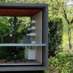 Thumbnail of http://A%20small,%20modern%20garden%20office%20cube%20with%20glass%20walls,%20a%20desk,%20chair,%20and%20shelves,%20surrounded%20by%20greenery.
