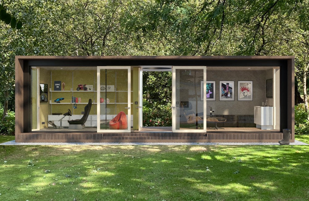 Modern garden office with glass walls, featuring a desk with a computer, a gaming chair, shelves with books and decor, a red beanbag, framed artwork, and a sofa, surrounded by trees and grass.