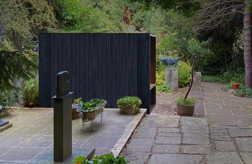 A modern black structure stands in a garden with stone paths, surrounded by green foliage and potted plants.