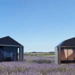 Thumbnail of http://Two%20modern,%20minimalist%20cabins%20with%20dark%20roofs%20stand%20in%20a%20lavender%20field%20under%20a%20clear%20blue%20sky.