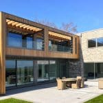 Thumbnail of http://Modern%20house%20with%20wooden%20and%20brick%20exterior,%20featuring%20large%20windows,%20a%20balcony,%20and%20a%20patio%20with%20outdoor%20furniture%20set.