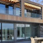 Thumbnail of http://Modern%20house%20exterior%20with%20large%20glass%20windows,%20wooden%20paneling,%20and%20a%20brick%20facade.%20Outdoor%20patio%20set%20with%20a%20round%20table%20and%20chairs%20in%20the%20foreground.