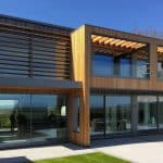 Thumbnail of http://Modern%20two-story%20house%20with%20large%20glass%20windows,%20wooden%20paneling,%20and%20a%20patio%20with%20outdoor%20furniture.