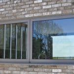 Thumbnail of http://A%20modern%20window%20with%20a%20sliding%20pane%20is%20set%20in%20a%20brick%20wall.%20The%20reflection%20shows%20outdoor%20trees%20and%20sky.