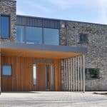 Thumbnail of http://Modern%20building%20exterior%20with%20brick%20and%20wood%20paneling,%20large%20windows,%20and%20a%20paved%20entrance.