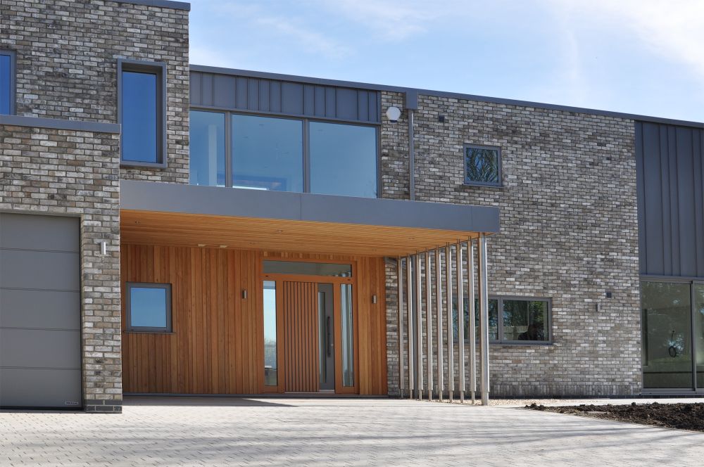 Modern building exterior with brick and wood paneling, large windows, and a paved entrance.