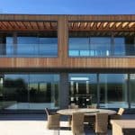 Thumbnail of http://Modern%20two-story%20house%20with%20wooden%20paneling%20and%20large%20glass%20windows.%20A%20round%20outdoor%20table%20with%20chairs%20is%20set%20on%20the%20patio%20in%20front.