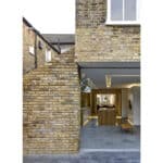 Thumbnail of http://Modern%20brick%20building%20with%20an%20open%20ground%20floor%20interior%20featuring%20a%20wooden%20bench%20and%20table,%20smooth%20concrete%20flooring,%20and%20large%20windows.