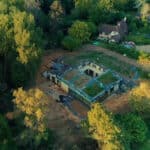 Thumbnail of http://An%20aerial%20view%20reminiscent%20of%20a%20Grand%20Designs%20project%20shows%20a%20partially%20constructed%20house%20with%20a%20green%20roof%20nestled%20among%20trees,%20alongside%20another%20home.