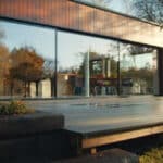 Thumbnail of http://This%20modern%20building,%20reminiscent%20of%20a%20Grand%20Designs%20project,%20boasts%20large%20glass%20windows%20that%20reflect%20the%20trees%20and%20clear%20sky.%20In%20the%20foreground,%20a%20wooden%20deck%20seamlessly%20blends%20with%20the%20lush%20greenery%20surrounding%20the%20structure.