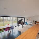 Thumbnail of http://Spacious%20modern%20living%20area%20reminiscent%20of%20Grand%20Designs,%20featuring%20a%20wooden%20counter,%20colorful%20chairs%20around%20a%20long%20table,%20a%20grand%20piano,%20and%20large%20glass%20doors%20opening%20to%20a%20garden%20view.