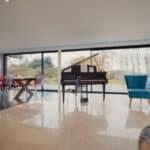 Thumbnail of http://This%20Grand%20Designs-inspired%20spacious%20modern%20living%20room%20features%20a%20grand%20piano,%20large%20windows%20revealing%20a%20scenic%20view,%20and%20a%20dining%20area%20adorned%20with%20colorful%20chairs.