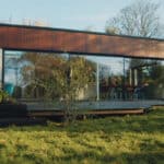 Thumbnail of http://A%20modern%20one-story%20house%20with%20large%20glass%20windows,%20reminiscent%20of%20a%20Grand%20Designs%20feature,%20is%20nestled%20within%20a%20lush%20grassy%20yard%20and%20surrounded%20by%20trees.