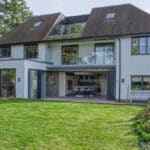 Thumbnail of http://Modern%20two-story%20house%20with%20large%20windows,%20glass%20balconies,%20and%20an%20open%20patio%20leading%20to%20a%20well-kept%20lawn%20and%20garden%20in%20front.