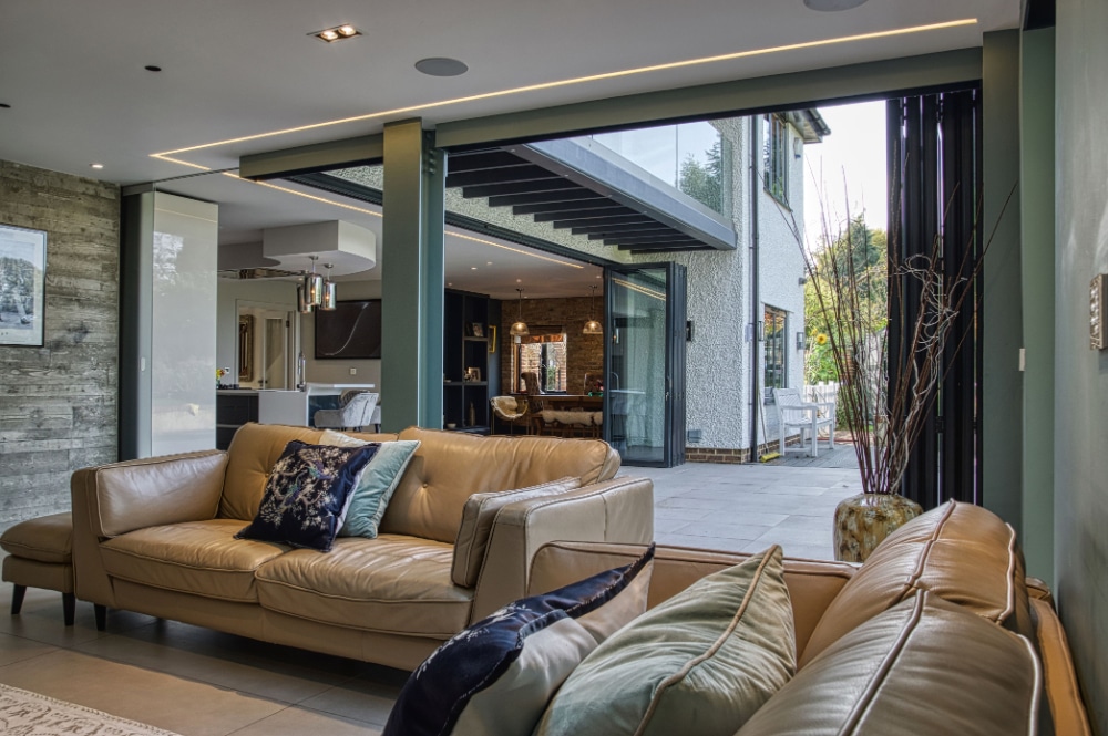 Modern living room with beige leather sofas, open sliding doors leading to a patio, and a view of the kitchen and dining area in the background.